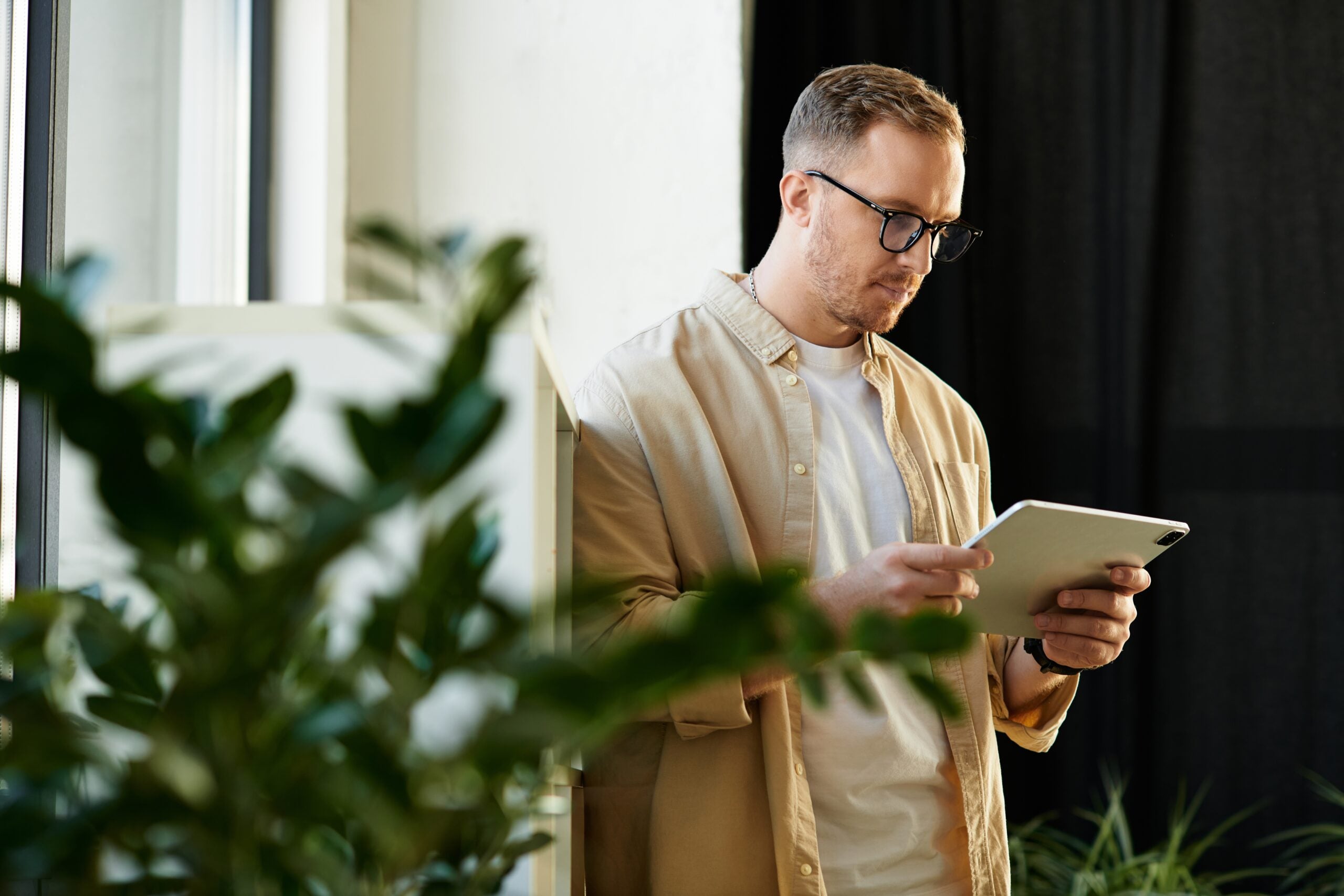 A young and handsome businessman is focused on his tablet, immersed in work in a modern office.