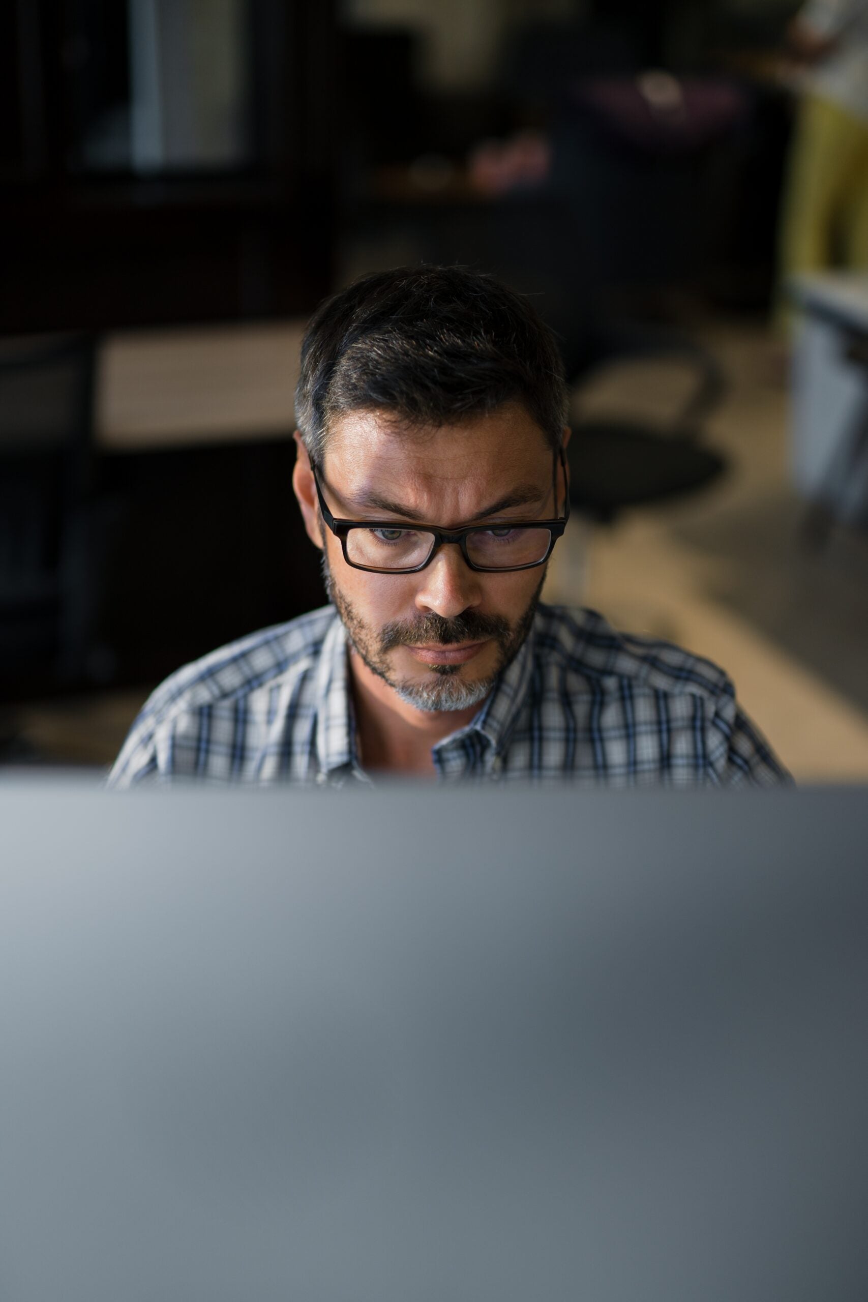 Man wearing glasses works on a computer at home, with a monitor screen reflected in his lenses.